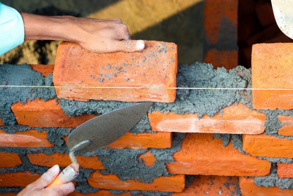 News Hands laying bricks with cement in a construction setting, showcasing precise masonry work.