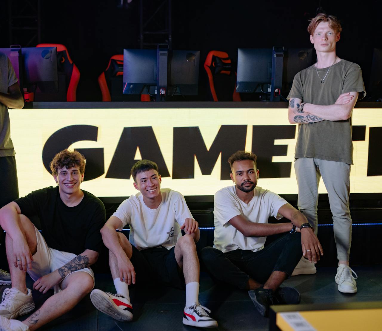 Four young men posing confidently in an eSports arena with gaming setups in the background.